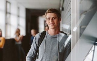 A young man in a grey sweatshirt looking into the camera smiling