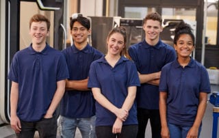 A group of young apprentices wearing blue shirts looking into the camera smiling