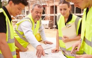 A group of people in yellow vests looking at a plan at a construction site
