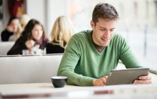 A young man sitting in a coffee shop looking at a tablet