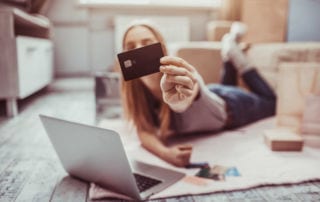 A young woman lying on the floor and holding up a credit card to the camera