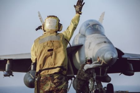 A military aviation mechanic signaling to a pilot on the deck of a carrier
