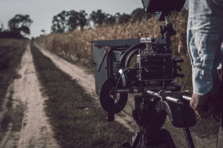 A closeup of a camera aiming down a road in a corn field