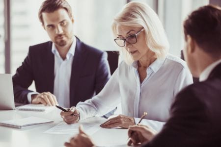 A woman talking to two men and looking at a piece of paper