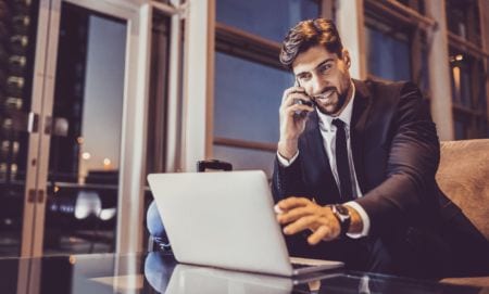A man talking on the phone and looking at a laptop