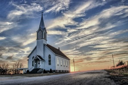 A small white church by a road at sunset