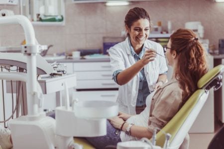 A young dental technician checking a woman's teeth in a dental chair