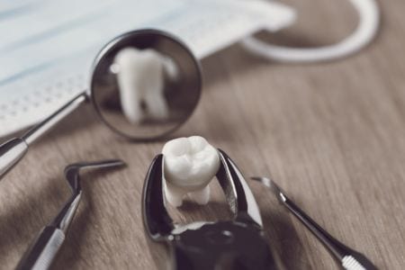 Pliers holding a tooth in front of a mirror