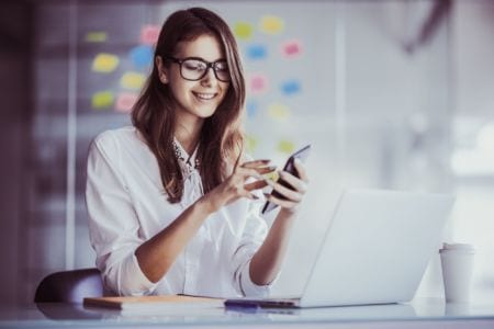 woman with glasses smiling with her phone in her hand reading an apprenticeship guide