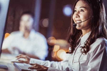 A smiling woman wearing headphones and looking at a screen