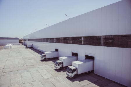 Four white trucks parked in the loading area of a hangar