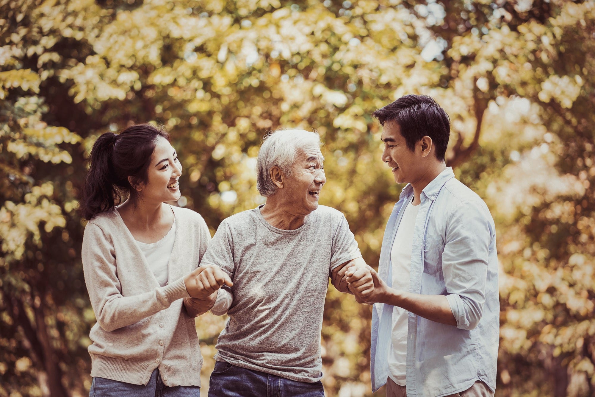 Two young people holding an elderly man's hands and smiling