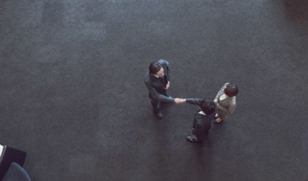 Aerial view of two people shaking hands standing next to a woman