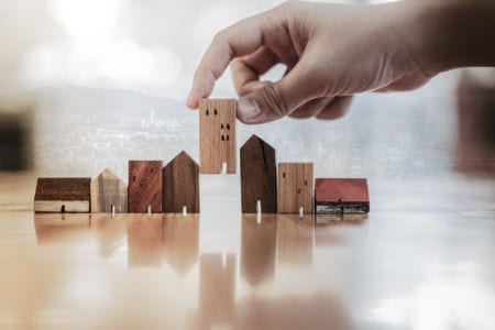A closeup of a hand holding a piece of wood shaped like a house