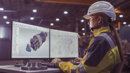 A manufacturing engineer wearing a helmet working on a computer