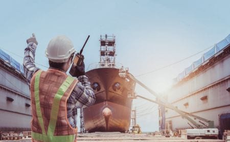 A marine surveyor holding a talkie walkie looking at a large ship