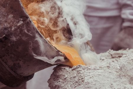 A closeup of a bucket pouring liquid metal into a mold