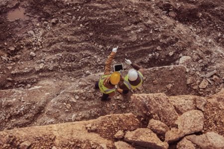 Aerial view of two industrial workers wearing reflective jackets standing on mining worksite outdoors using a tablet