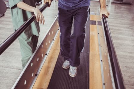 A patient holding on to parallel bars next to a doctor