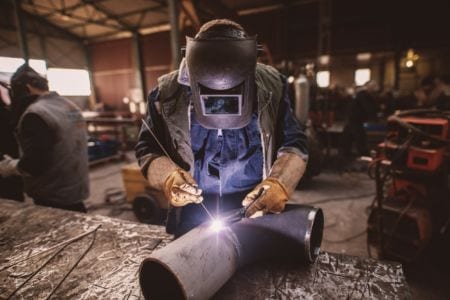 Welder in protective uniform and mask welding a metal pipe