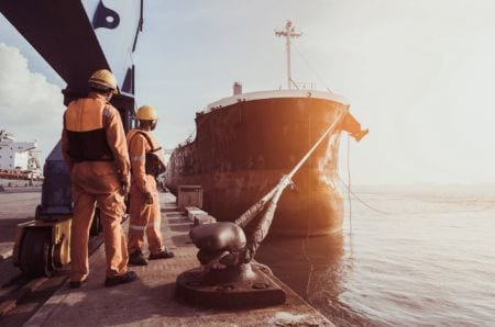 Container ship being unloaded with harbor dock workers standing next to it