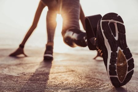 Back view of an athlete with a prosthetic leg starting to run outdoors