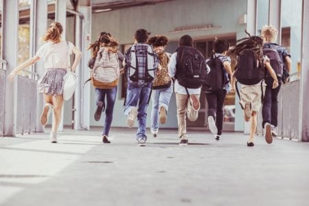 A group of kids wearing backpacks running towards the school entrance
