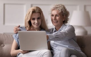 A senior mother and her daughter sitting on a couch looking at a laptop