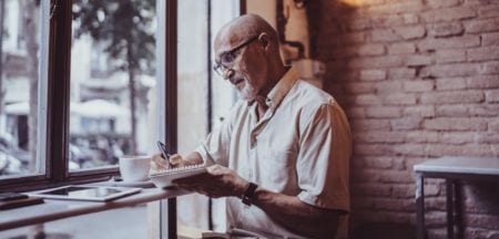 An elderly man writing notes in a coffee shop