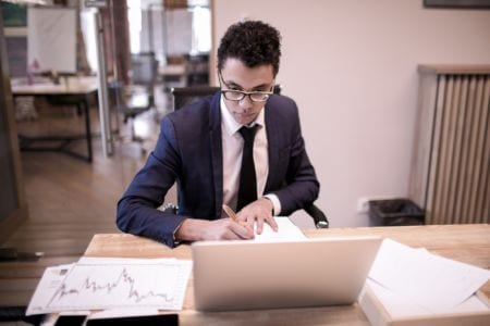 A young man writing notes in front of a laptop