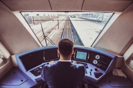 A train cockpit interior with the driver sitting and driving the train