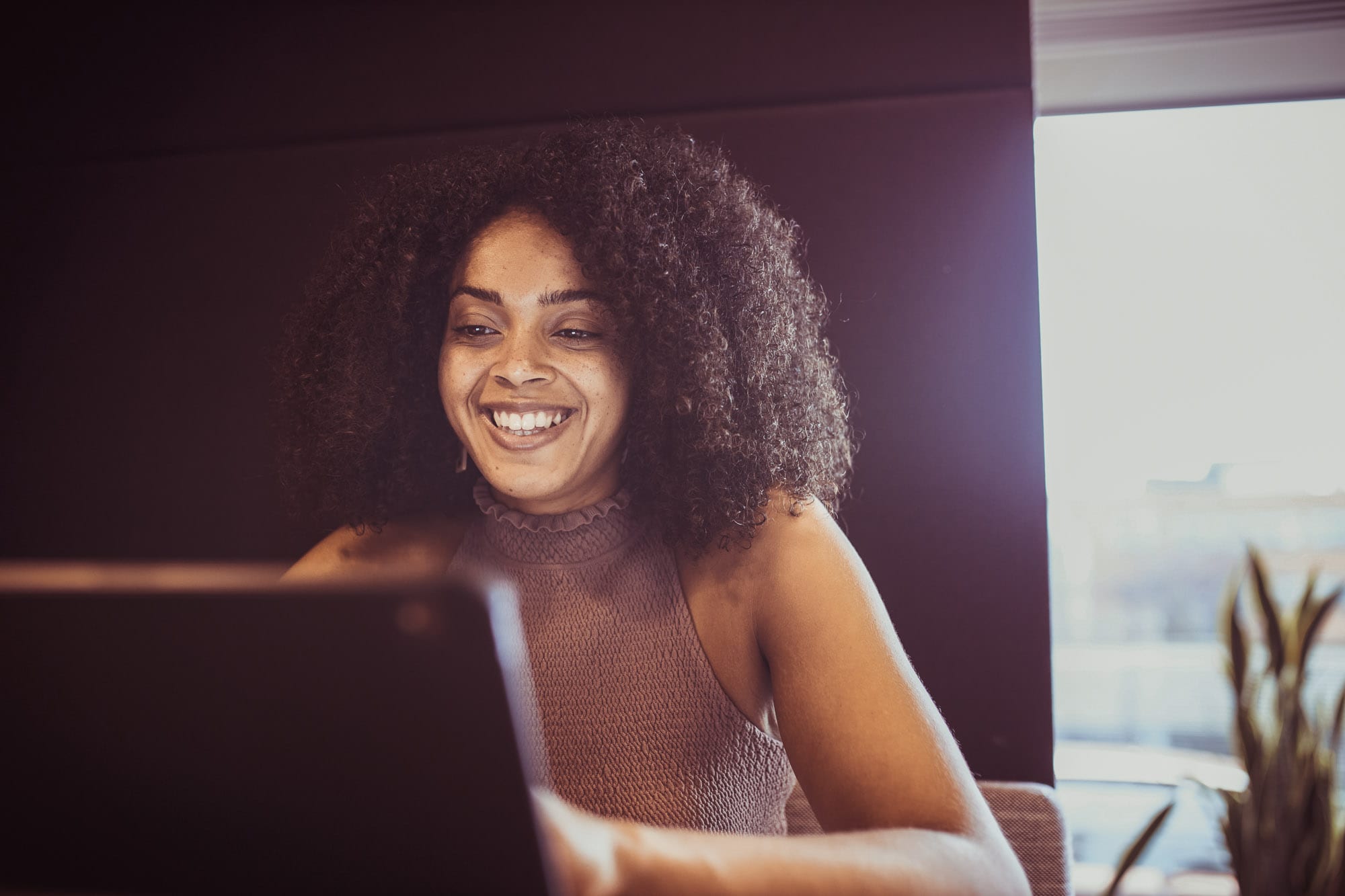 How to Become a Journalist - A young woman looking at a laptop smiling