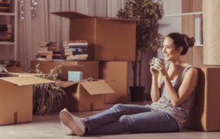 A young woman sitting on the floor smiling while surrounded by boxes