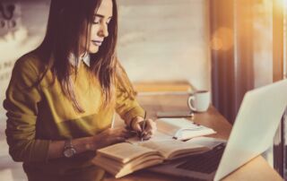 Woman writing her notes down in front of a laptop