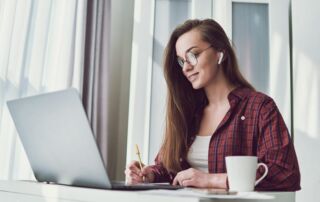A young woman sitting and writting in front of a laptop while smiling